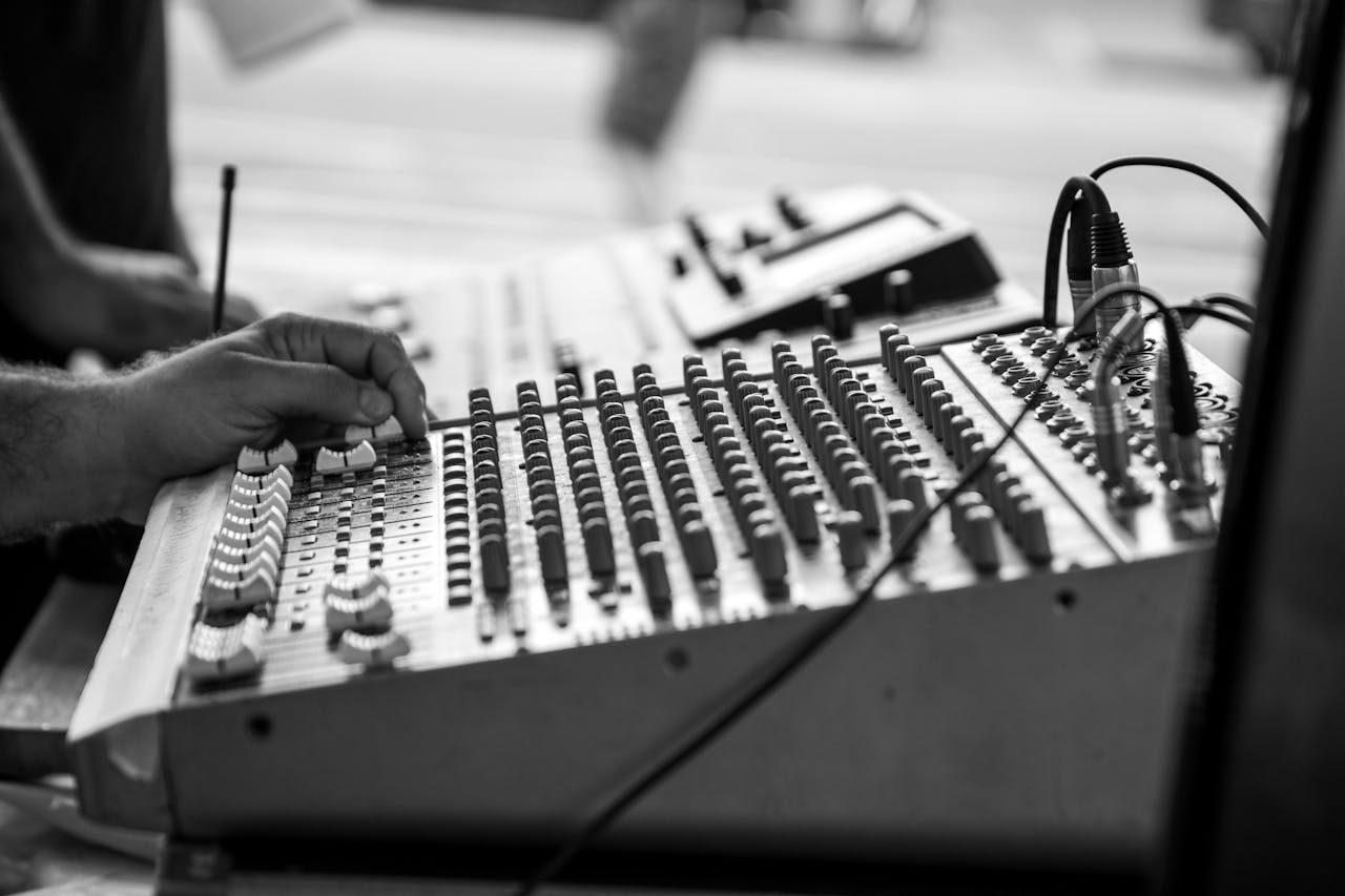 gallery-2 Black and white image of hands operating a sound mixer with knobs and wires.